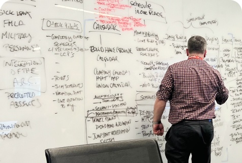 A team member standing at a whiteboard covered in handwritten notes mapping crew member workflows